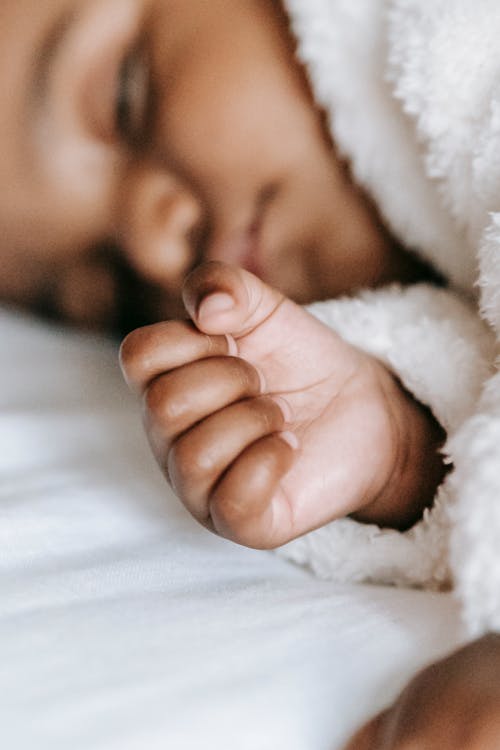 Free Crop adorable innocent African American baby in warm clothes sleeping on comfortable bed in daylight at home Stock Photo
