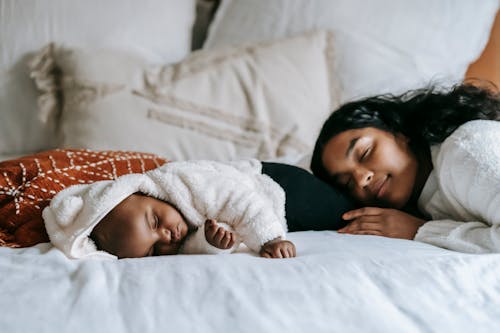 Side view of young African American mother and cute baby sleeping together on comfortable bed in morning