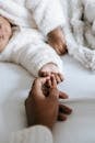 High angle of crop unrecognizable African American woman holding hand of newborn baby baby sleeping on soft bed in daylight