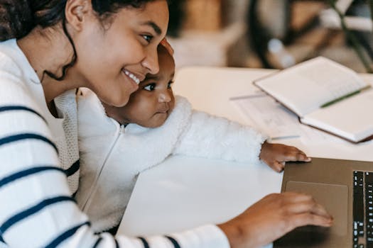 Smiling mother multitasks with laptop while holding her child, highlighting work-life balance.