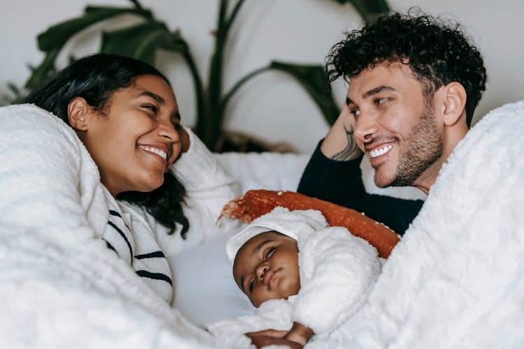 Happy Ethnic Couple Lying With Baby On Bed In Bedroom