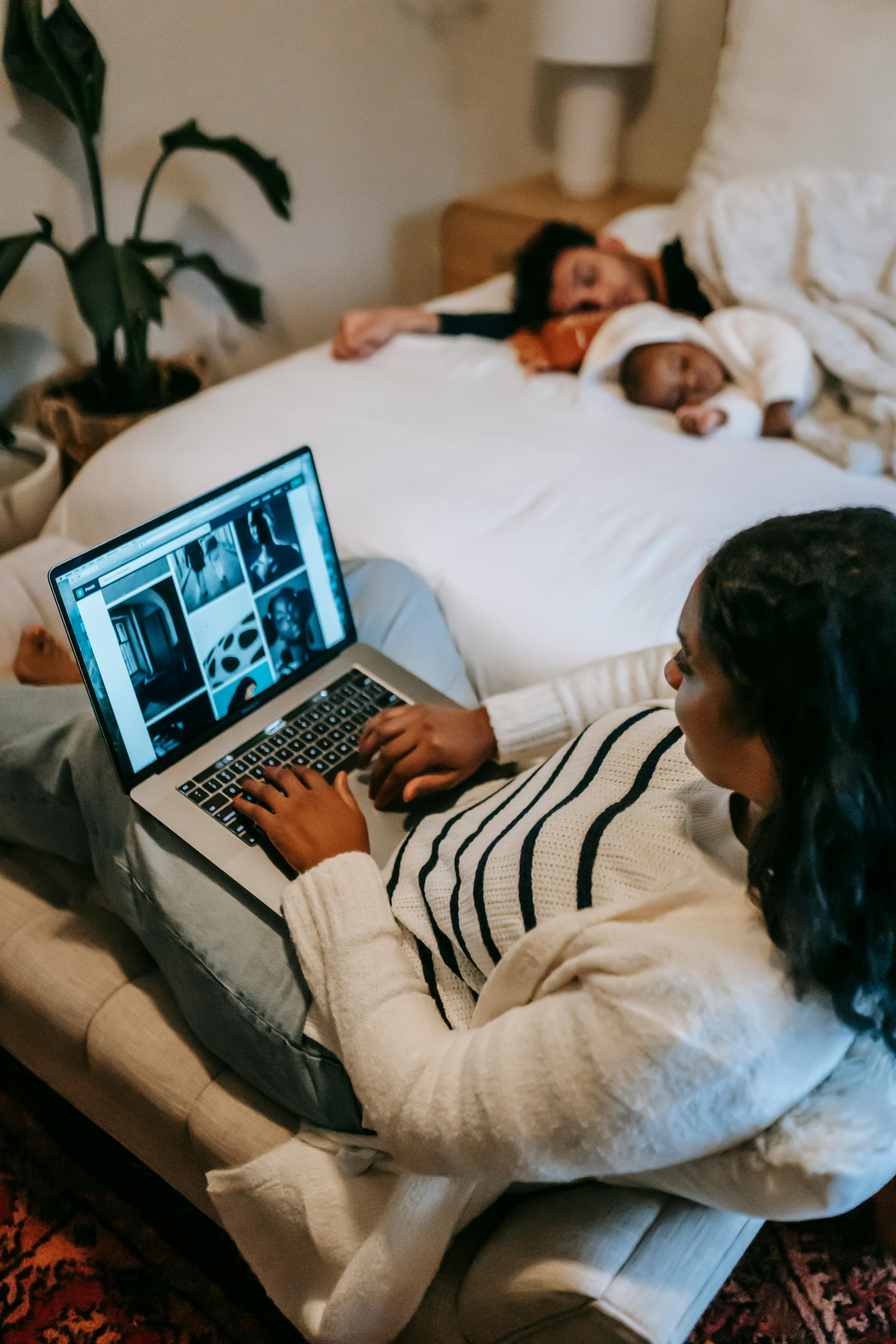 woman freelancer working on netbook while husband and baby sleeping on bed