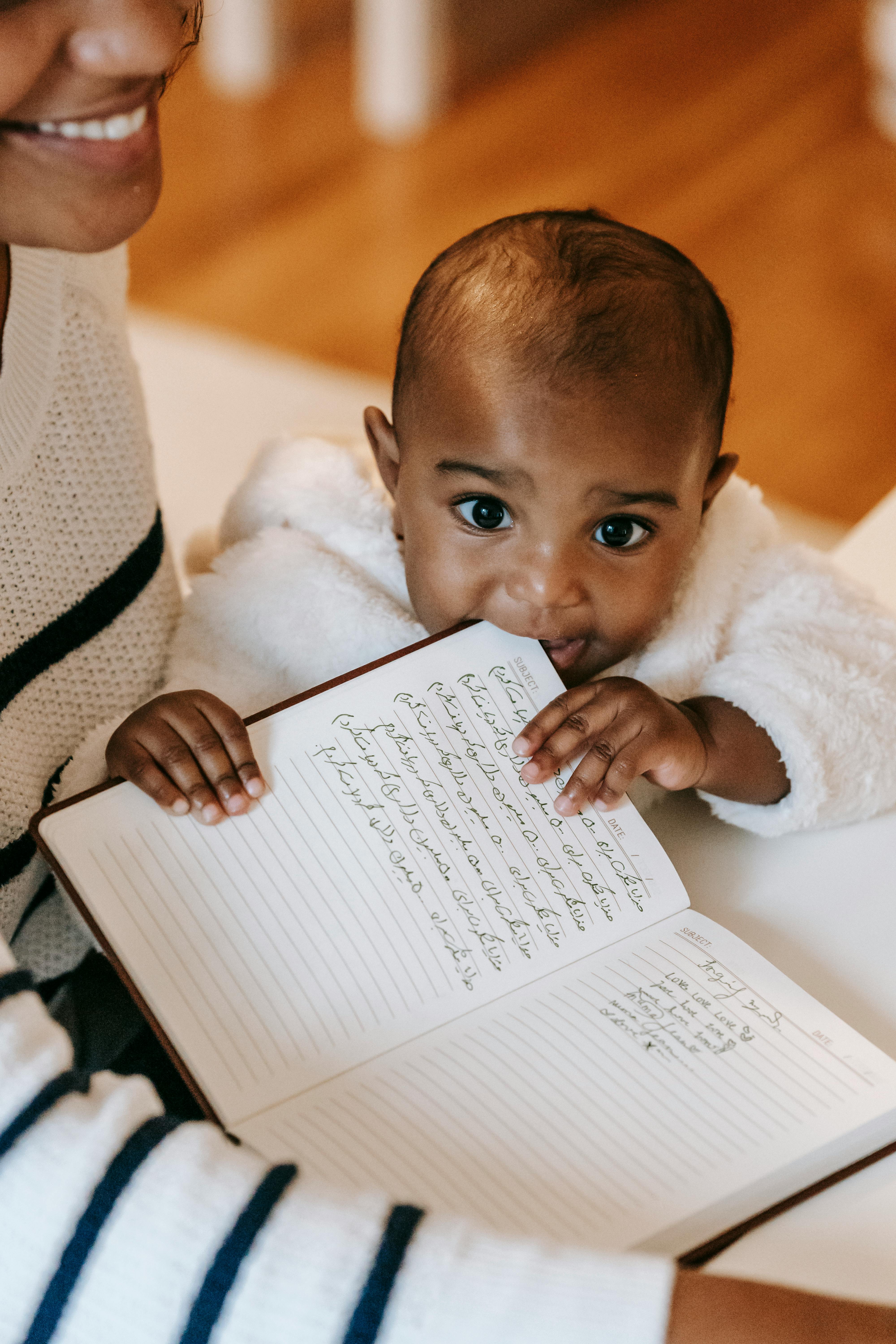 ethnic baby biting notebook in daytime