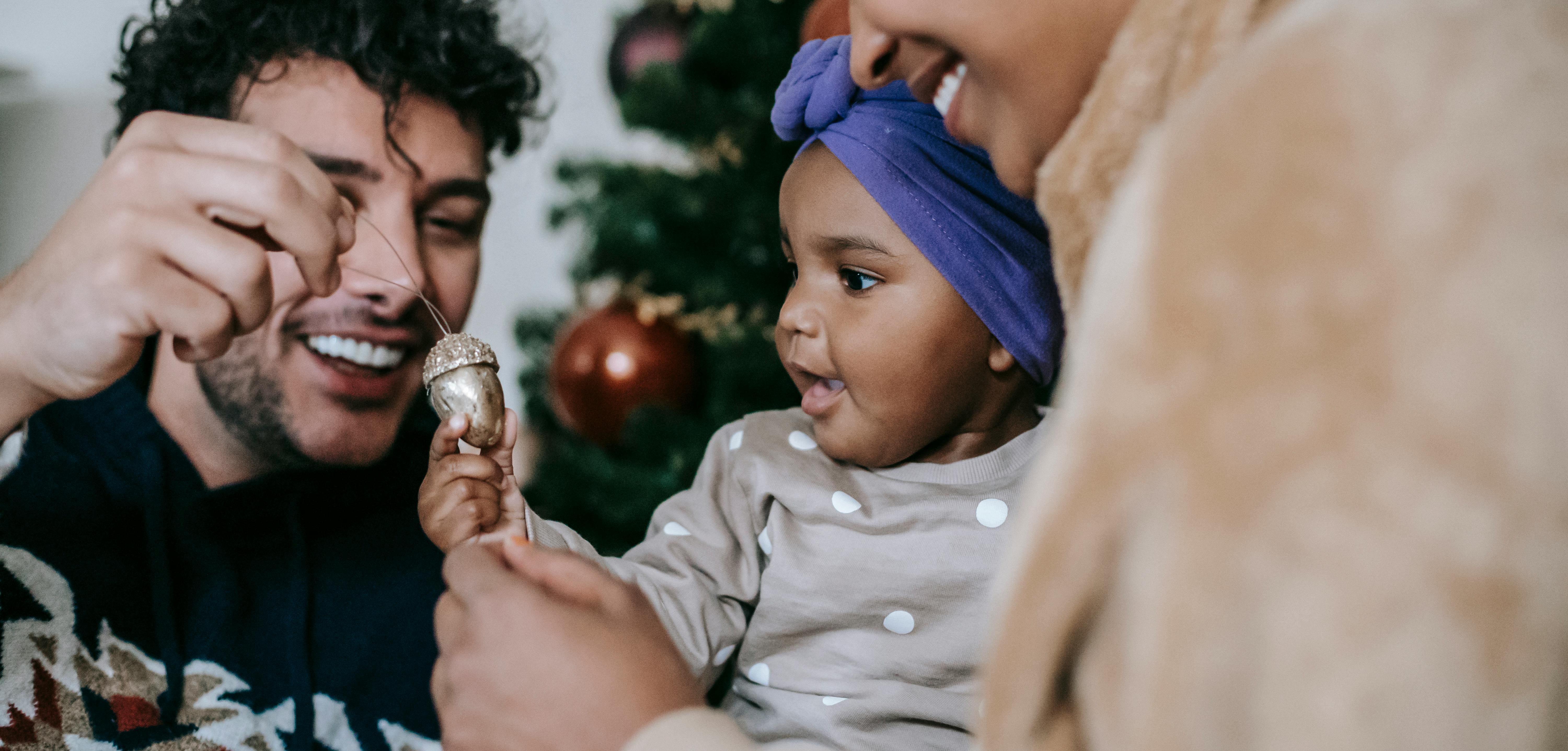 happy ethnic couple playing with baby against christmas tree at home