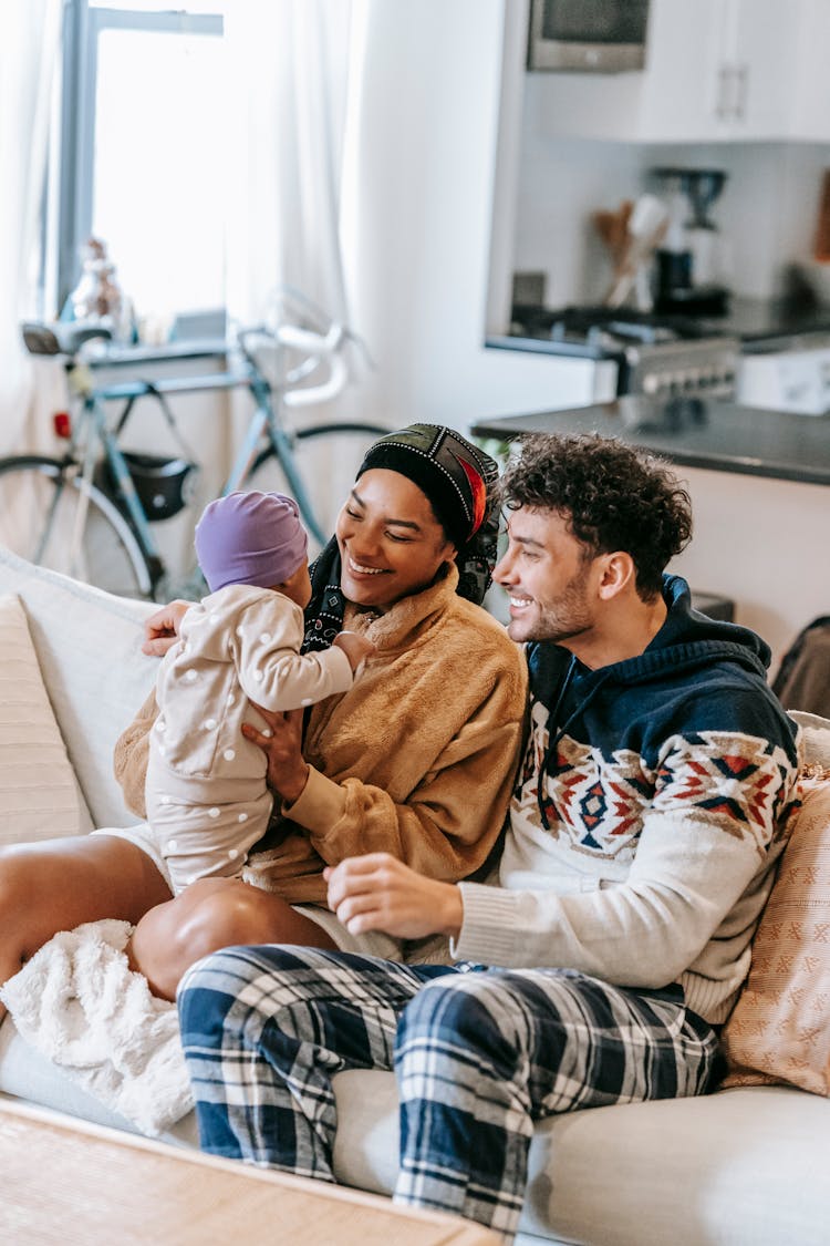 Happy Ethnic Couple Sitting With Baby On Sofa At Home