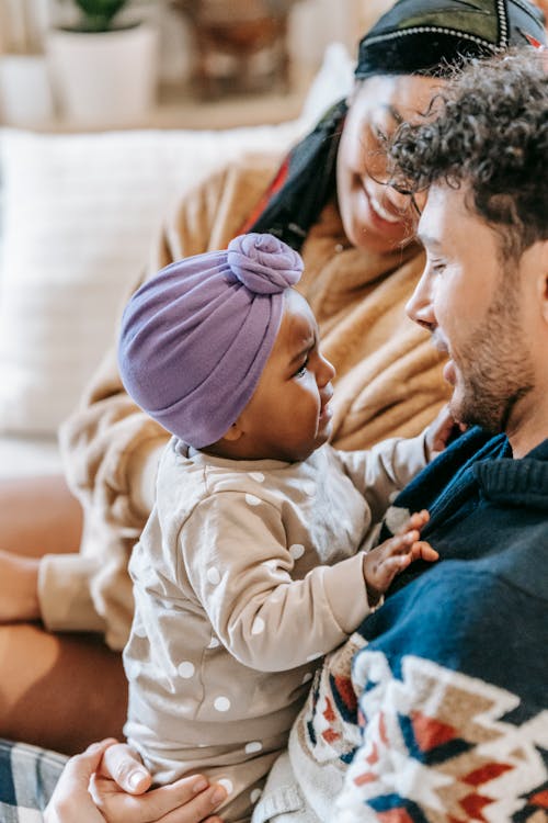 Side view of cheerful multiethnic parents with crying African American baby siting on couch in living room on blurred background