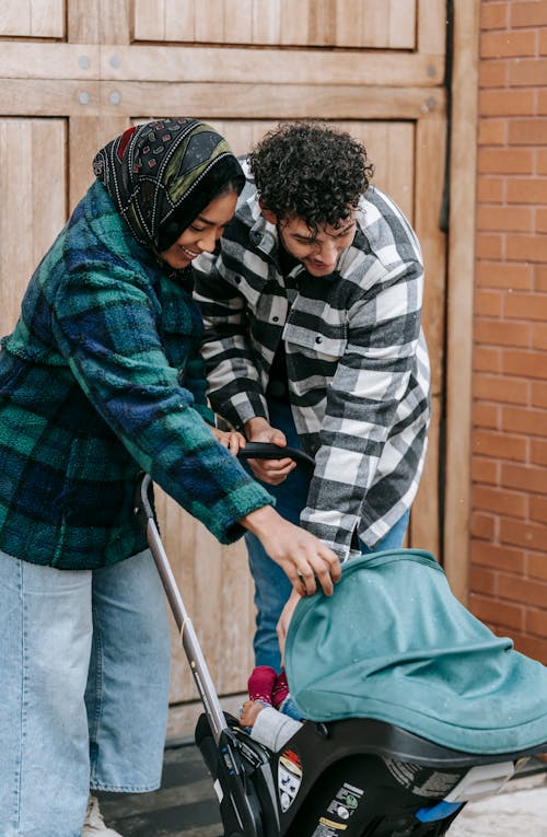 Positive African American mother and father standing near baby sitting in baby carriage on street in city near building