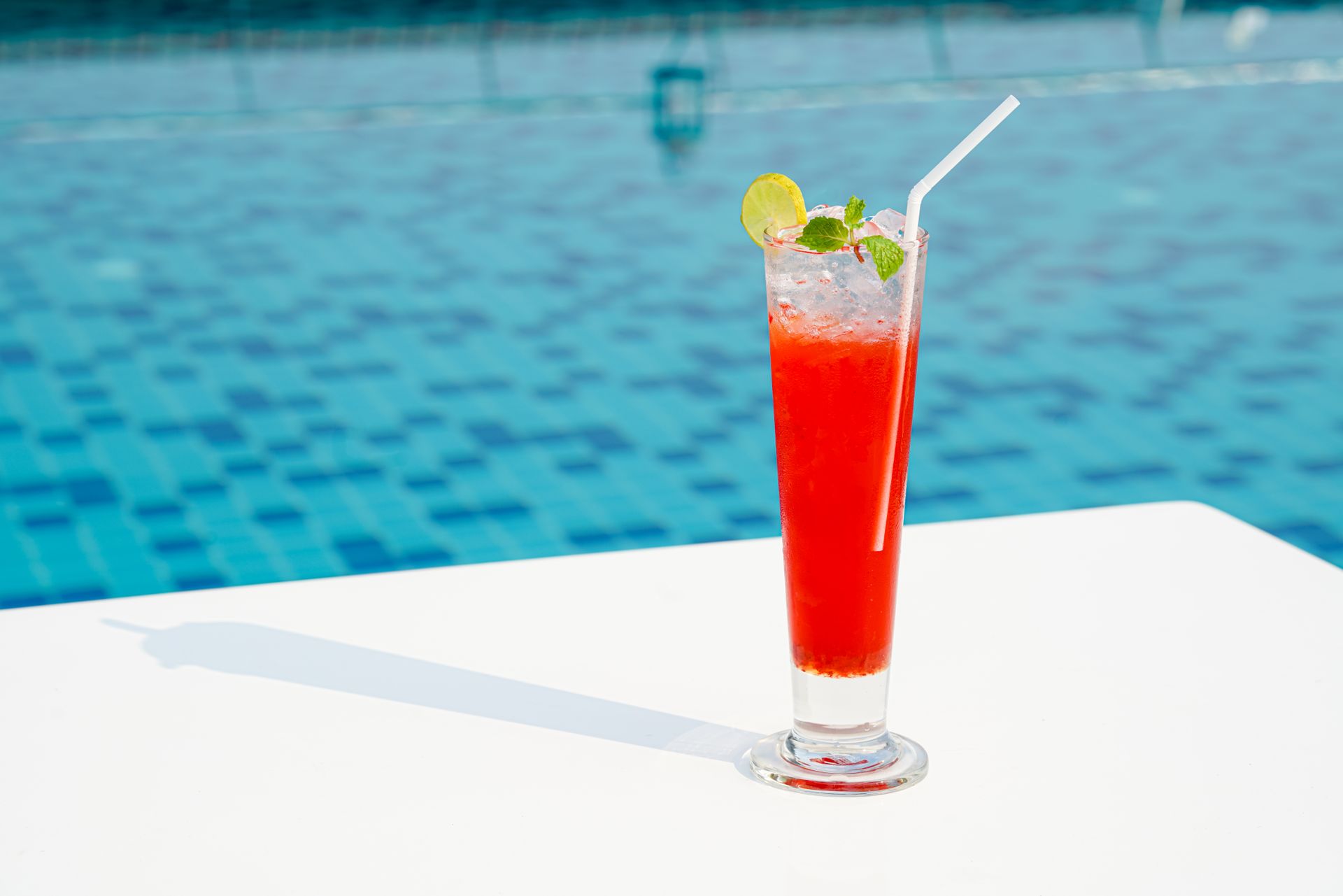 Enjoy a refreshing strawberry cocktail with ice and mint by the pool on a sunny day.