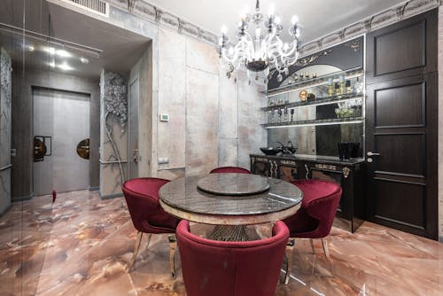 Interior of modern spacious kitchen with round table and red chairs placed near contemporary counter with kitchenware in stylish apartment