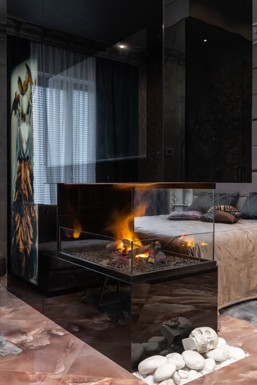 Free Transparent glass fireplace with bright flame placed on tiled floor with stones near bed in modern cozy bedroom at home Stock Photo
