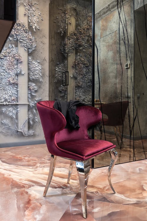 Comfortable red armchair with black textile placed on floor near wall with decorative elements in room with mirror at home
