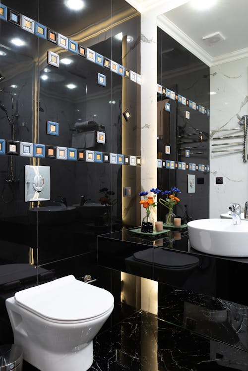 Interior of modern restroom with black tiled wall with sink placed on marble surface with flower near white bidet at home