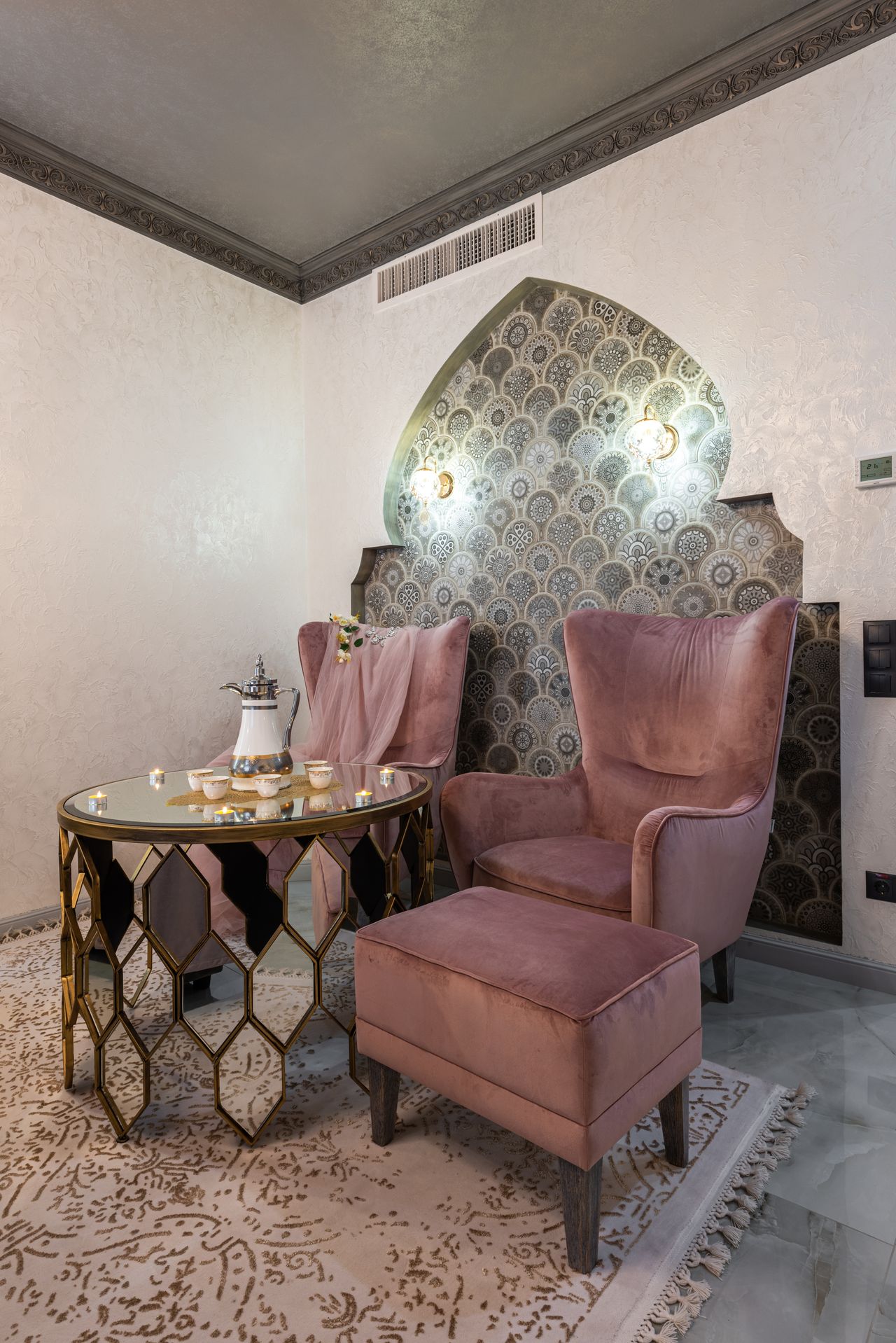 Glass table with teapot and cups between two pink armchairs