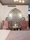 Stylish bedroom with comfortable bed and side table with set of cups and teapot placed between pink armchairs near ornamental wall