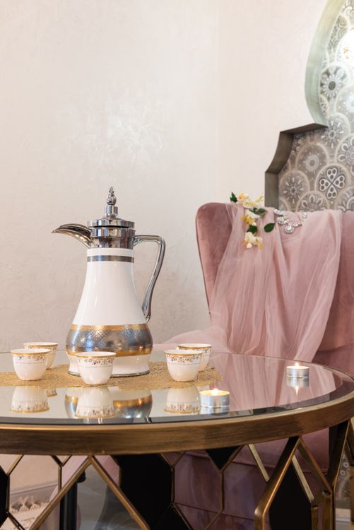 Bộ đồ trà sứ phương Đông — ấm trà và cốc sứ nhỏ bày cùng nến thơm trên bàn kính phản chiếu, không khí thư giãn spa wellness