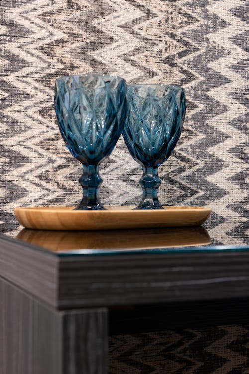 Similar blue glasses with decorative ribbed surface on wooden tray reflecting on table against wall in house