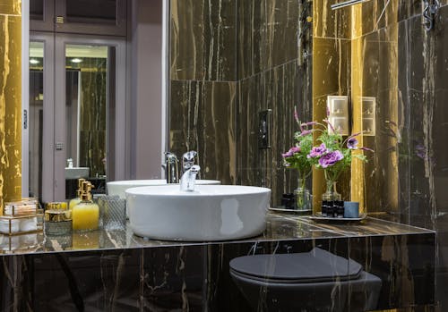 Free Contemporary bathroom with washstand between decorative flowers and liquid soap reflecting in mirror against door Stock Photo