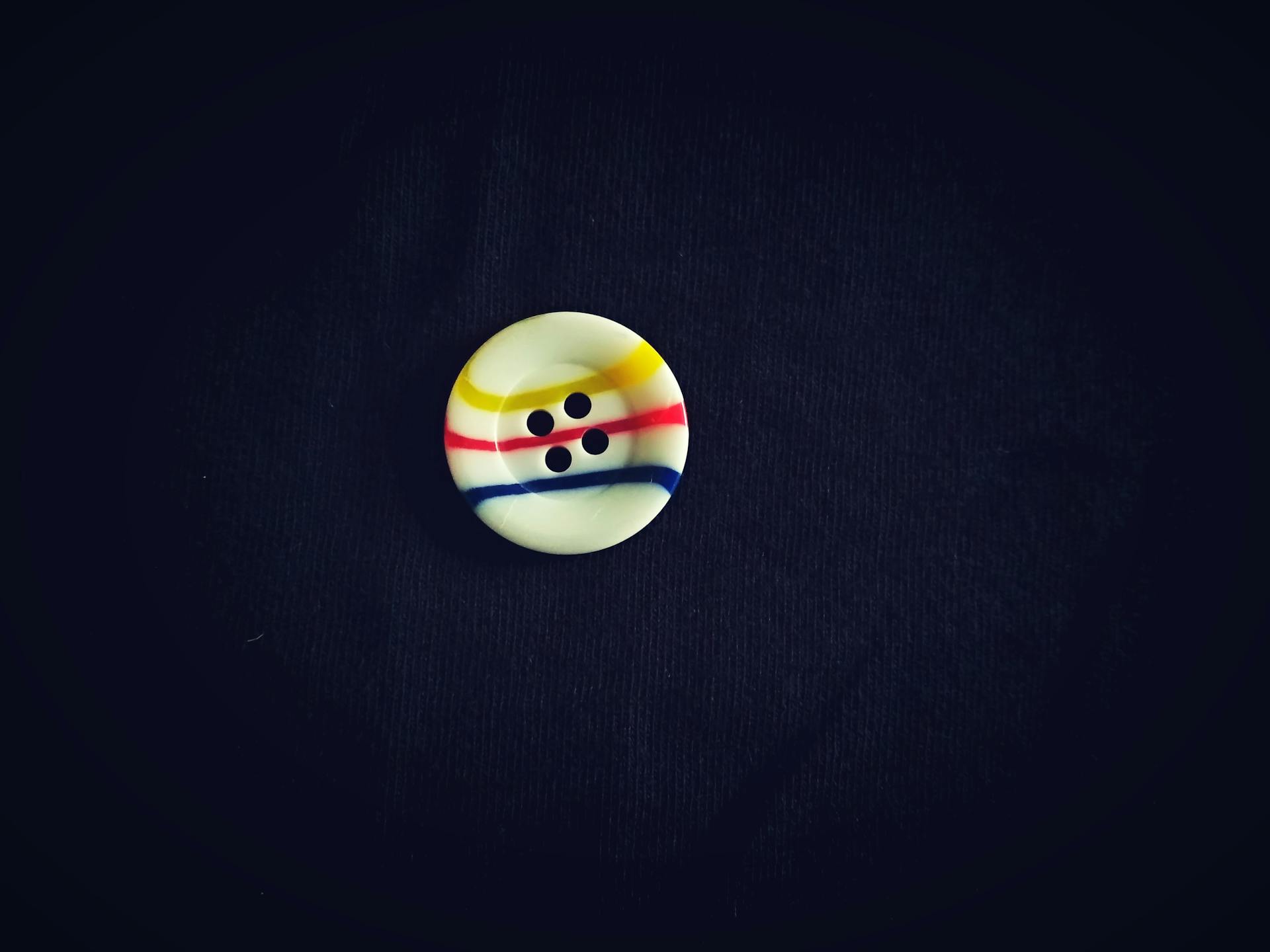 Close-up of a round button with colorful stripes against a black fabric backdrop.