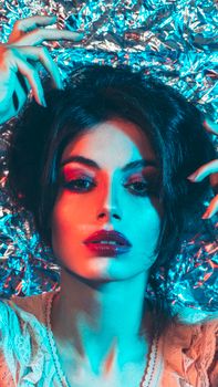 Striking portrait of a woman with colorful lighting and silver foil background.