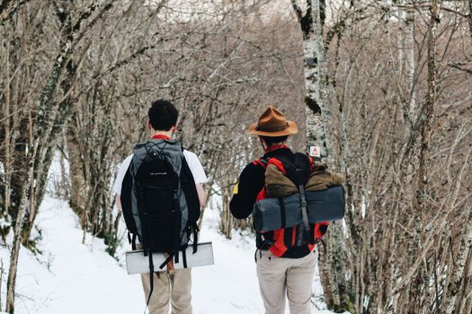 Two men hiking in a snow-covered forest, showcasing winter adventure and exploration.