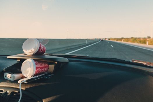 Dashboard view with coffee cups on a road trip in Slovakia, capturing the open highway and clear sky for travel enthusiasts.