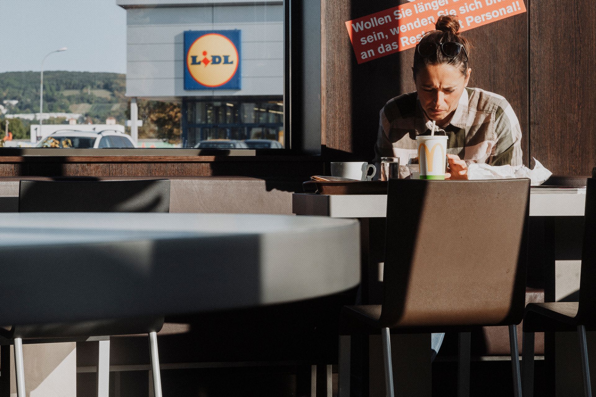 A person enjoying a meal indoors, with Lidl supermarket visible outside through the window.