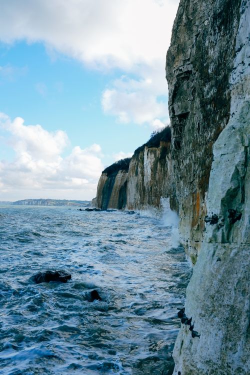 Free Scenic view of rough rocky cliff washed by foamy sea waves under clear blue sky Stock Photo