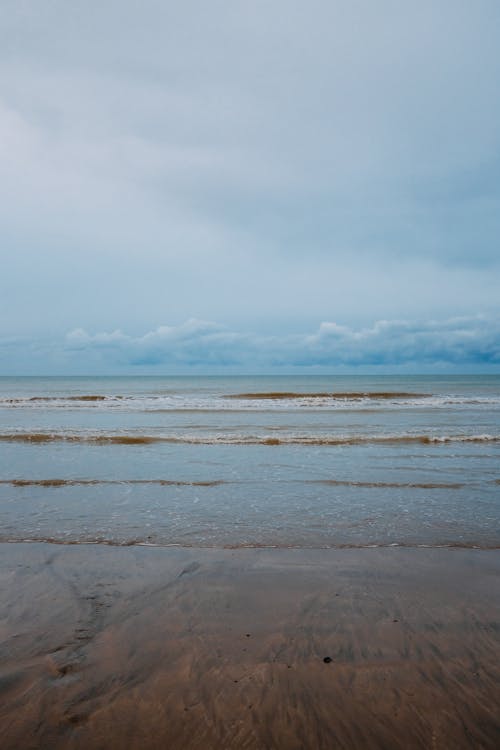 Free Waving sea near sandy shore on overcast day Stock Photo