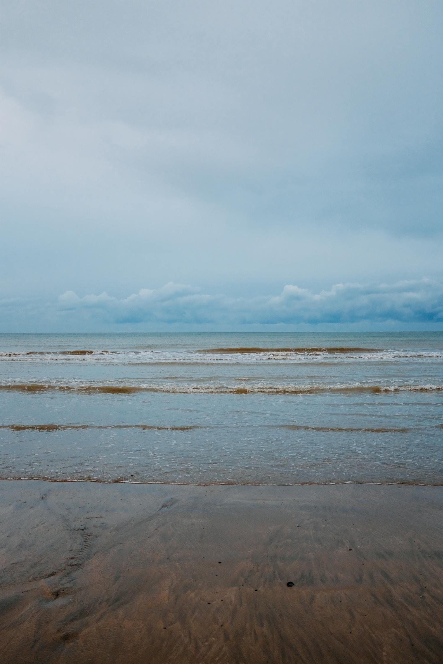 Waving Sea Near Sandy Shore On Overcast Day · Free Stock Photo
