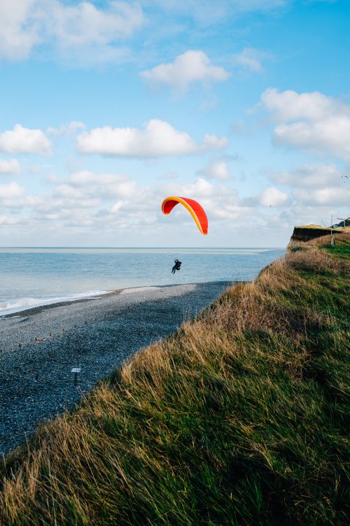 Free Faceless paraglider flying over sandy beach and peaceful blue seawater under blue sky Stock Photo