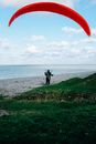 Back view anonymous paraglider landing on grassy seashore near endless scenic sea under clear blue sky