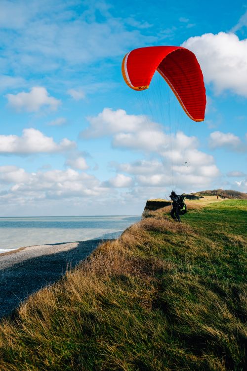 Free Full body unrecognizable paraglider landing on lush grassy seacoast beneath clear blue sky Stock Photo