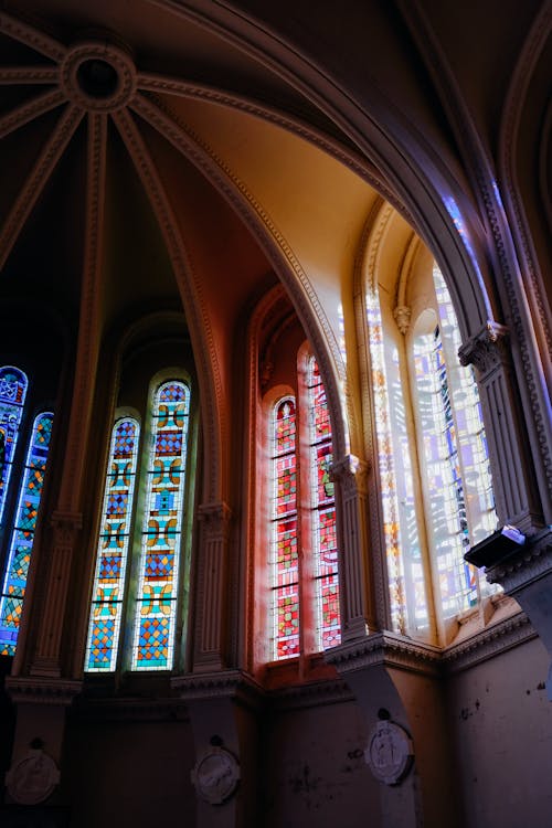 Low angle historic church dome with colorful leaded glass windows under arched ceiling in sunlight