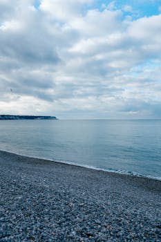 Serene ocean view with a pebble beach under cloudy skies, conveying tranquility.