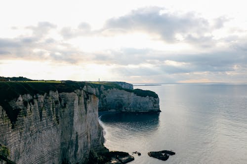 Free Rocky cliff with verdant moss near calm water of endless ocean under cloudy sunny sky Stock Photo