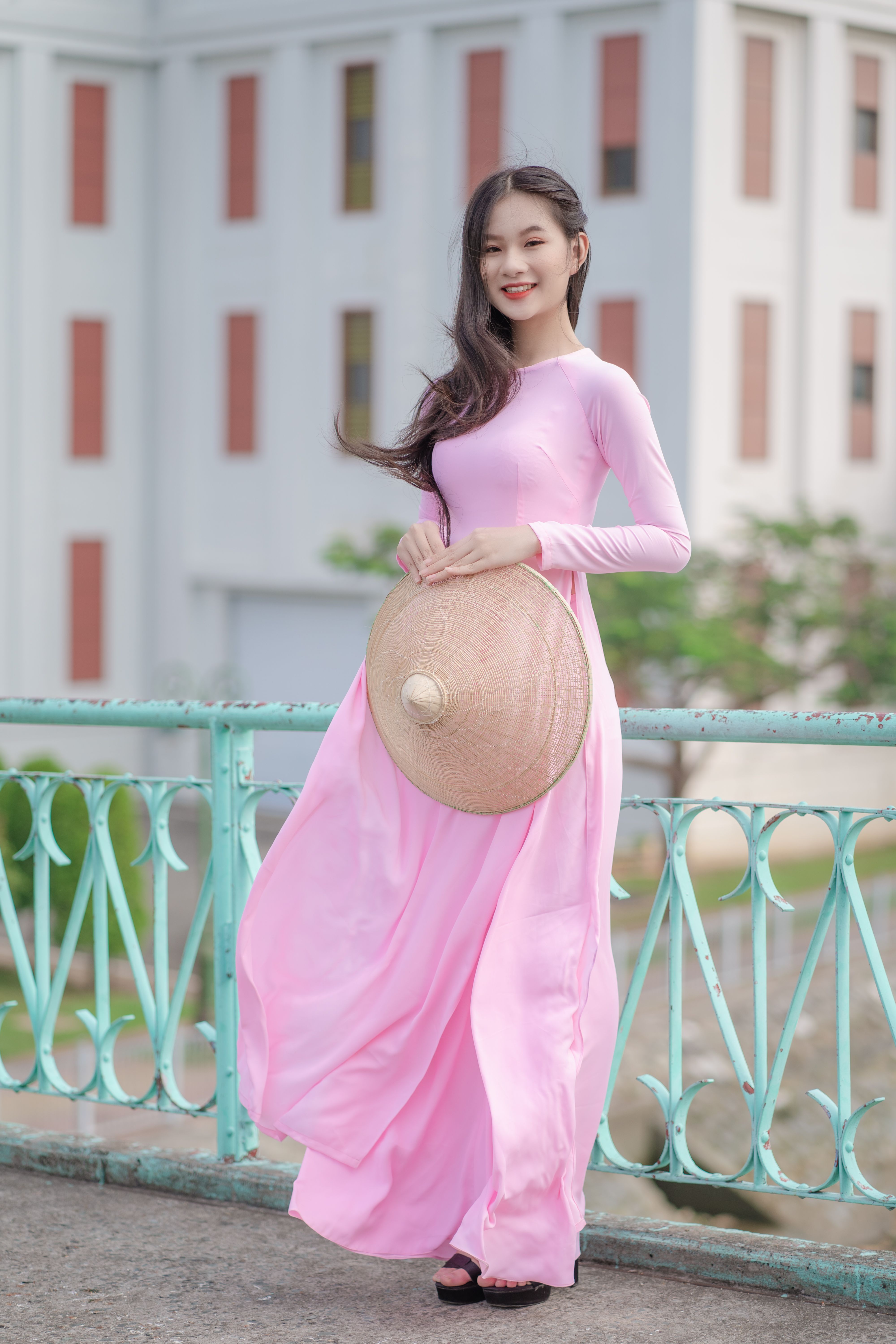 Young woman smiling in a pink dress, holding a hat outdoors, evoking elegance and grace.