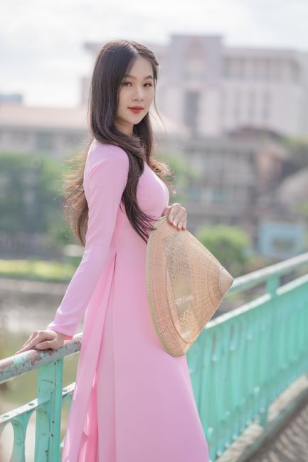 Asian woman in a pink dress holding a sakkat, posing elegantly outdoors.