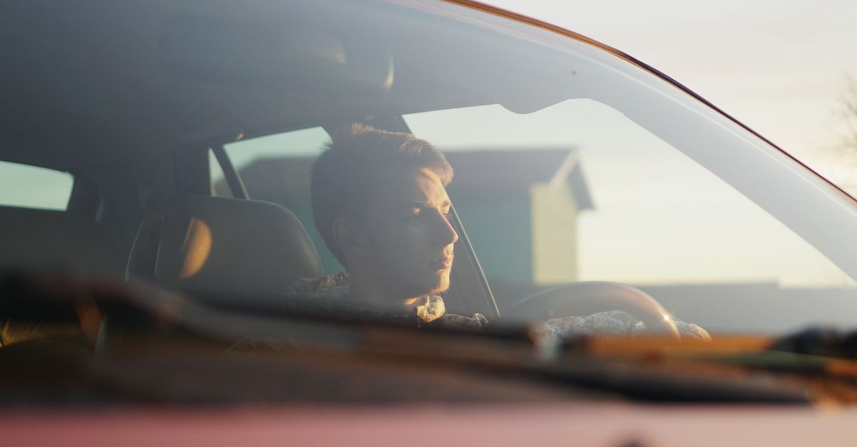 Um homem dirigindo um carro com a luz do sol iluminando o interior através do para-brisa.