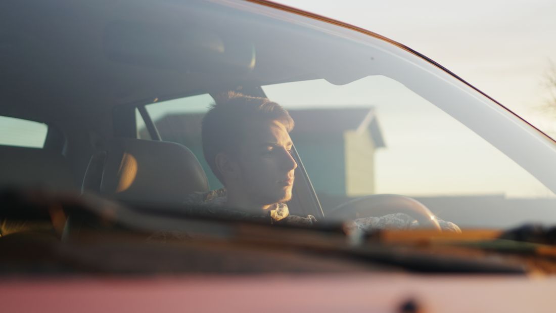 A man driving a car with sunlight illuminating the interior through the windshield