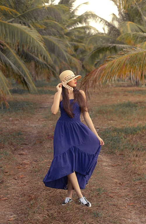 蓝色的裙子，戴着白色的太阳帽，站在绿色的草地上的女人