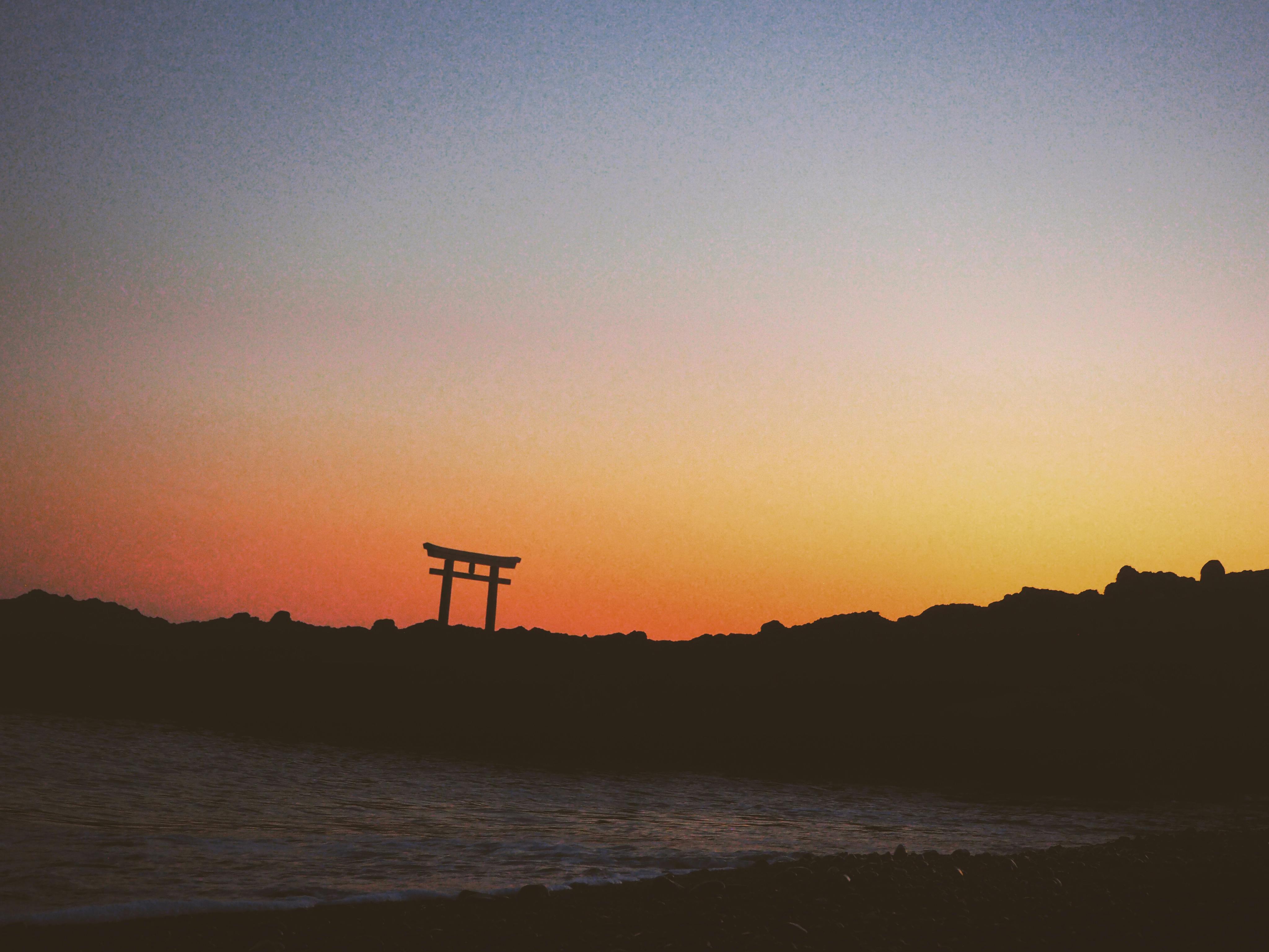 Serene silhouette of Torii gate over Tokyo horizon at twilight with soft color gradients.