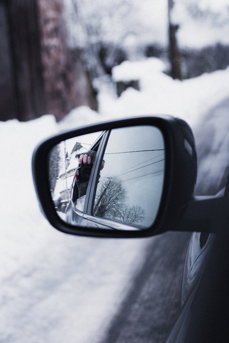 Reflection In Car Side Mirror Of Anonymous Person Taking Selfie During Trip In Winter