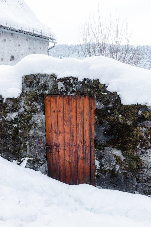 Small weathered stone shack with wooden door located on snowy terrain in rural area in countryside in cold winter day