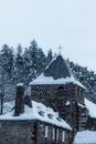 Aged chantry exterior with cross on top against fir trees with snow in countryside on winter day