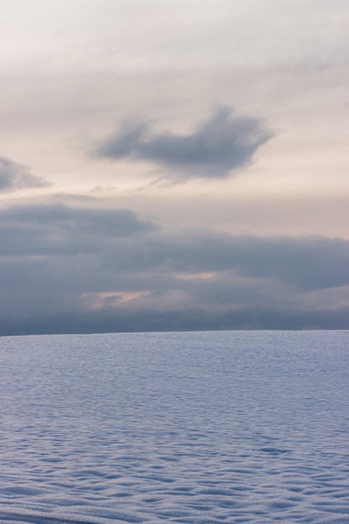 Scenic view of snowy land with wavy surface under cloudy sky in countryside at sunset