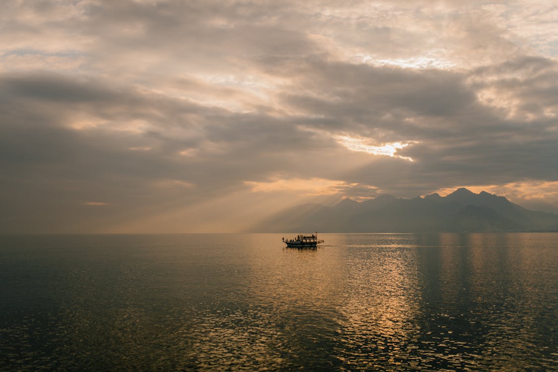 Free Picturesque scenery of boat floating on rippling water of sea against amazing cloudy sunset sky Stock Photo