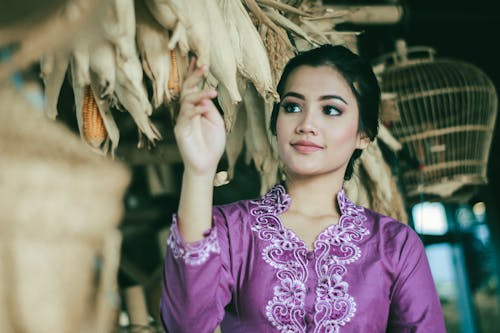 
A Woman Wearing a Purple Traditional Clothing Looking at Hanged Corn