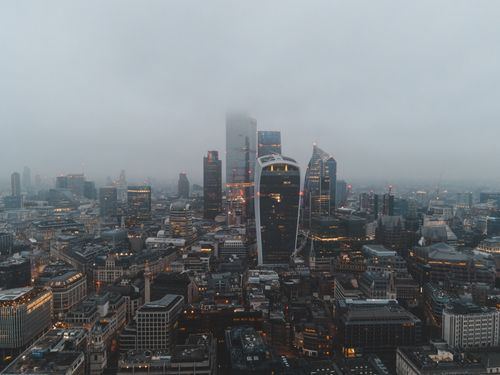 Free Drone view of city with modern buildings and skyscrapers under gray cloudy sky in foggy evening Stock Photo