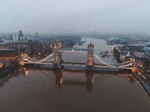 Free Aerial view of London city located in England with illuminated Tower Bridge on River Thames near modern buildings under gray cloudy sky in foggy day Stock Photo