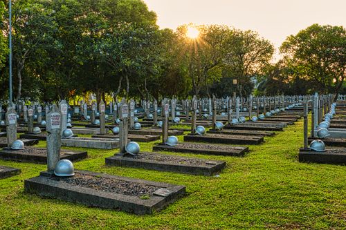 Free Rows of tombstones with military helmets located on grassy ground near tall lush green trees in heroes cemetery in Kalibata Stock Photo
